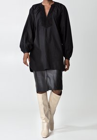 Svart långärmad tunika med en texturerad v-ringning, kombinerad med en svart läderpennkjol och krämfärgade knähöga stövlar.