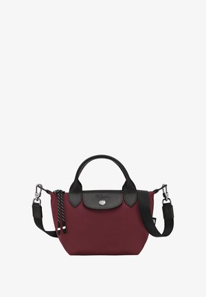 Burgundy tote bag with black leather accents, featuring a top handle, adjustable strap, and silver snap closure. Textured fabric finish.
