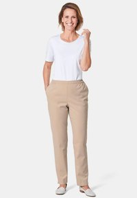 Un pantalon beige à taille élastique associé à une chemise blanche à manches courtes, présentant une coupe décontractée et une texture lisse. Les chaussures sont des mocassins blancs.
