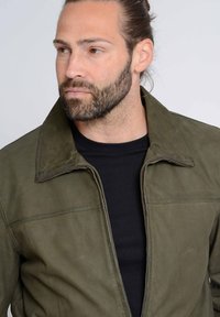 Olivgrüne Lederjacke mit strukturiertem Kragen, Reißverschluss und subtilen Nähten. Das Model trägt ein schwarzes T-Shirt darunter.