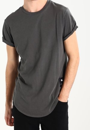 Graues Baumwoll-T-Shirt mit umgeschlagenen Ärmeln, Rundhalsausschnitt und abgerundetem Saum. Verfügt über ein kleines Markenzeichen an der Seite. Glatte Textur.
