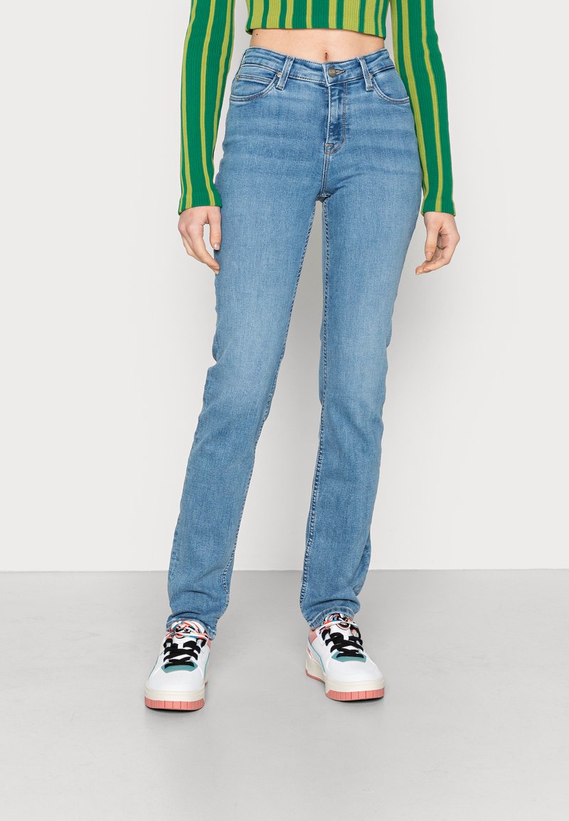 Jeans blu chiaro a vita alta con vestibilità dritta, leggermente sbiaditi e design a cinque tasche standard, abbinati a sneakers bianche.