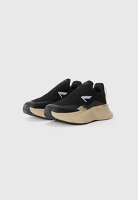 Black athletic shoes with a slip-on design, textured upper, and a beige sole. Features a subtle pattern and logo accents on the sides.