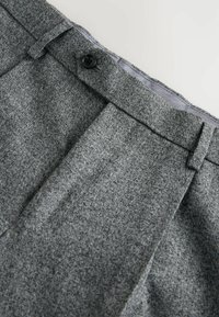Graue Textilhose mit einem gefalteten Vorderdesign, ausgestattet mit einem schwarzen Knopfverschluss und einem subtilen Fischgrätmuster.