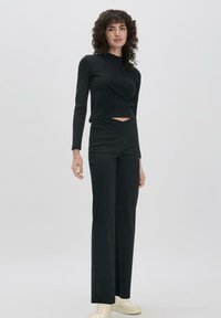 Zweiteiliges Outfit in Schwarz, bestehend aus einem figurbetonten Langarmoberteil mit Ausschnitt und hochgeschnittenen, geraden Hosen. Glatte Textur.