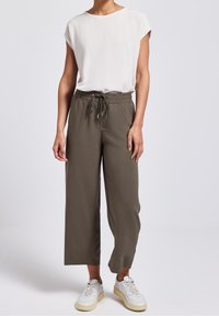 Cream short-sleeve top paired with olive green, loose-fitting cropped pants featuring an elastic waistband and drawstring. White sneakers complete the look.