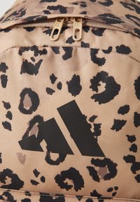 Leopard print backpack with a light beige base, black spots, and a prominent black triangle logo. Features dual zippers for opening.