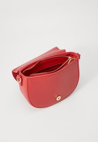 Röd konstläderväska med rundad form, gulddetaljer på dragkedjan och säker tryckknappsstängning. Insidan har flera fack.