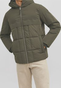 Giacca imbottita verde oliva con cappuccio, caratterizzata da trapuntatura orizzontale, chiusura frontale con zip e tasche laterali. Realizzata in materiale liscio e impermeabile.