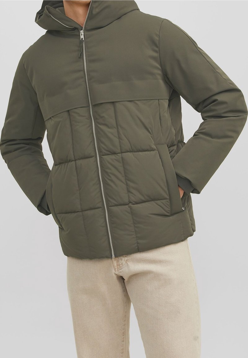 Giacca imbottita verde oliva con cappuccio, caratterizzata da trapuntatura orizzontale, chiusura frontale con zip e tasche laterali. Realizzata in materiale liscio e impermeabile.