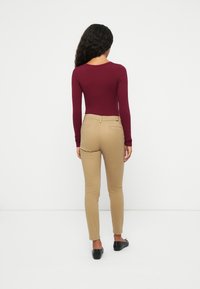 Bodysuit bordeaux à manches longues associé à un pantalon kaki ajusté. La tenue présente une texture de tissu lisse et un design minimaliste.