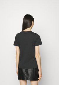 Czarny bawełniany t-shirt z krótkim rękawem i okrągłym dekoltem, noszony z czarną skórzaną spódnicą, widok z tyłu na białym tle.