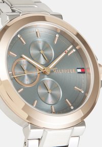 Montre en acier inoxydable argenté avec un boîtier en or rose, un cadran bleu-gris, trois petits sous-cadrans et des accents en cristal. Présente un design classique.