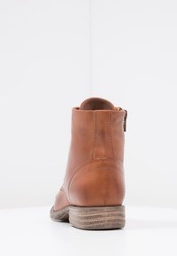 Stivaletto in pelle marrone con tacco basso impilato, dettaglio con zip sul lato, texture liscia e design della punta rotonda.