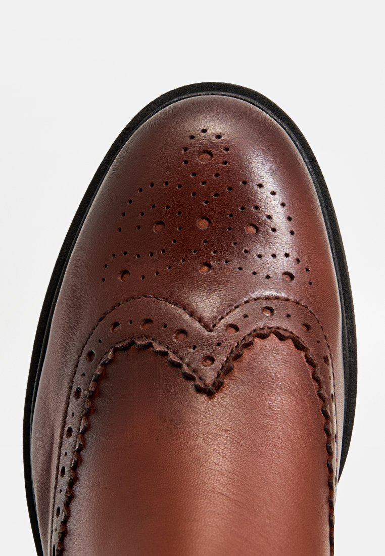 Braunes Leder Schuh mit einer runden Zehenform, ausgestattet mit Broguemuster, Perforationen und einer schwarzen Gummisohle. Glatte Textur und dezenter Glanz.