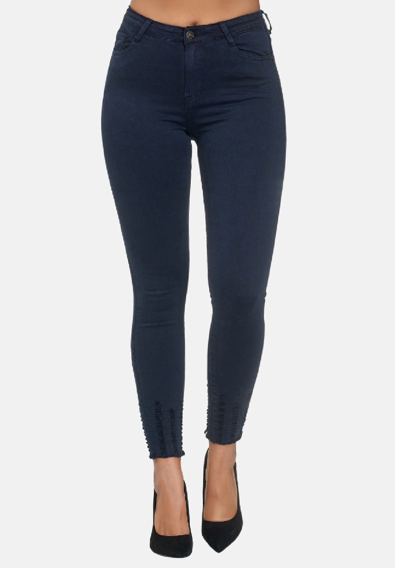 Jeans ajustados de mezclilla azul oscuro, con una cinturilla de altura media, bolsillos frontales y detalles texturizados en los dobladillos de los tobillos. Tacones altos negros.
