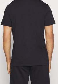 T-shirt nera in cotone con maniche corte, vestibilità rilassata e collo a giro. Il retro presenta una texture liscia e solida senza motivi visibili.