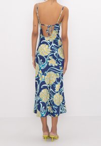 Robe midi bleu marine avec un motif floral en jaune et bleu canard. Elle possède des bretelles fines, un dos nu avec des liens et une silhouette fluide.
