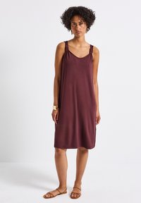 Burgundy ärmlös klänning med elastiska axelband, mjukt tyg, avslappnad passform och medellång design. Buren med minimaliska sandaler.