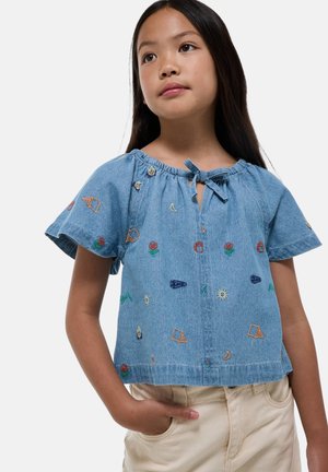 Top en denim avec des manches courtes évasées, un col rond et une fermeture à nouer. Présente des broderies florales et géométriques colorées sur l'ensemble.