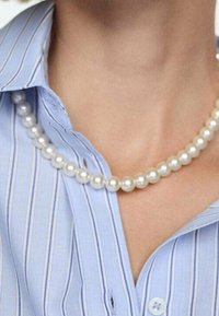 Un collier de perles blanches repose sur un col à rayures verticales bleues et blanches ; il présente des perles lisses, rondes et de taille uniforme.