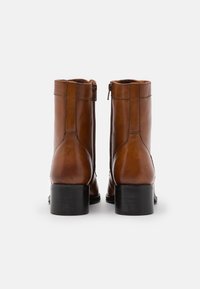 Bottines en cuir marron avec une texture lisse, fermeture zippée, talon noir et coutures renforcées, présentées de l'arrière.