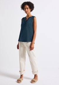 Top senza maniche color navy con scollatura henley e tasca frontale, abbinato a pantaloni crema con risvolto e sandali beige intrecciati da infilare.