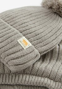 Grijze gebreide beanie met ribbeltextuur, afgewerkt met een pompoen. Heeft een rechthoekig label met een berenafbeelding en de tekst "GA BUITEN ONTDEKKEN."