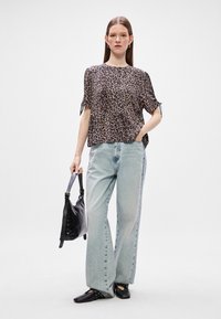 Μπλούζα κοντομάνικη με λεοπάρ σχέδιο και δεμένες μανίκες, σε συνδυασμό με ανοιχτό μπλε παντελόνι σε φαρδιά γραμμή και μαύρες επίπεδες παπούτσια, κρατώντας μια μαύρη τσάντα ώμου.