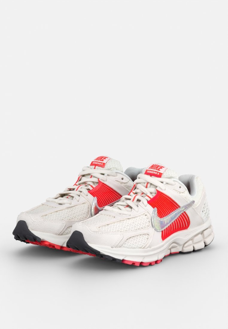 Baskets de running Nike avec une tige en mesh crème, des accents textiles rouges, un swoosh argenté et une semelle en caoutchouc noire. Design léger et respirant.