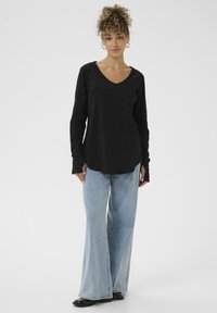 Zwart langemouwen top met V-hals, gecombineerd met lichtblauwe wijde jeans. De outfit heeft een losse pasvorm en zachte texturen.
