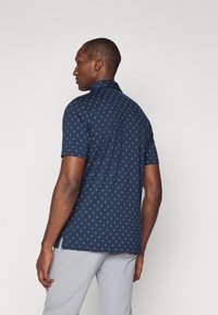 Polo de manga corta en azul marino con un patrón de estrellas verdes claras repetido, textura suave y diseño de cuello clásico.