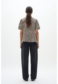 Top a maniche corte con stampa leopardata, dal taglio dritto, abbinato a pantaloni in denim neri, larghi e con tasche posteriori.