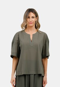 Blusa verde oliva a maniche corte con scollatura a V e una leggera lucentezza. Vestibilità rilassata, texture liscia e orlo dritto. Nessun motivo o dettaglio visibile.