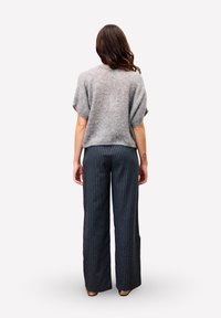 Grijze cropped trui met korte mouwen, gecombineerd met donkergestreepte wijde broek. De trui is zacht en heeft een textuur, terwijl de broek een op maat gemaakte pasvorm heeft.