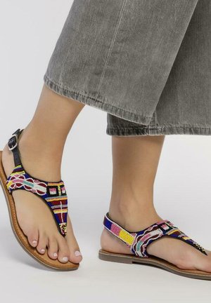 Sandalias de cuentas con patrones multicolores, correas de cuero negras y una suela marrón; el diseño incluye un separador de dedos y soporte para el tobillo.