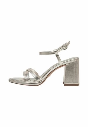 Metallic zilveren sandaal met hoge hak, een vierkante teen, drie gekruiste bandjes en een stevige hak. Verstelbare enkelband met metalen gesp.