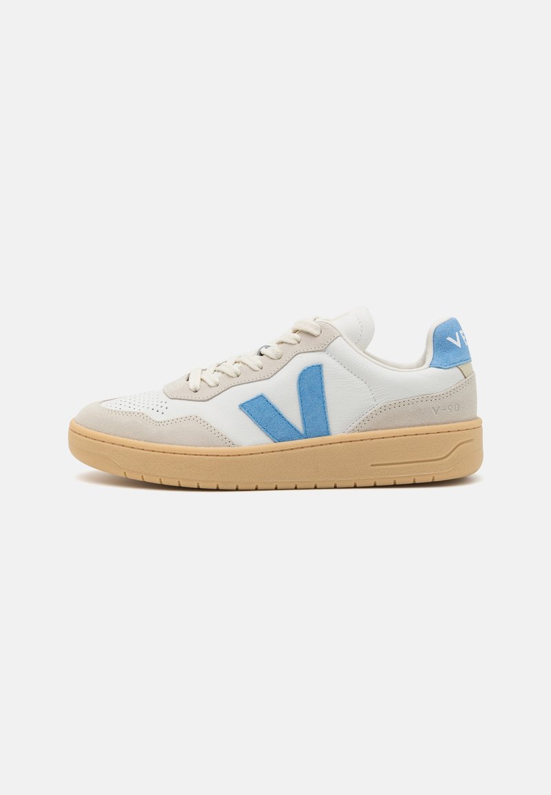 Hvit sneaker med lys grå semsket skinn detaljer og en blå filt-logo. Har en teksturert tåhette og en beige gummisåle. Klassisk lavt design.