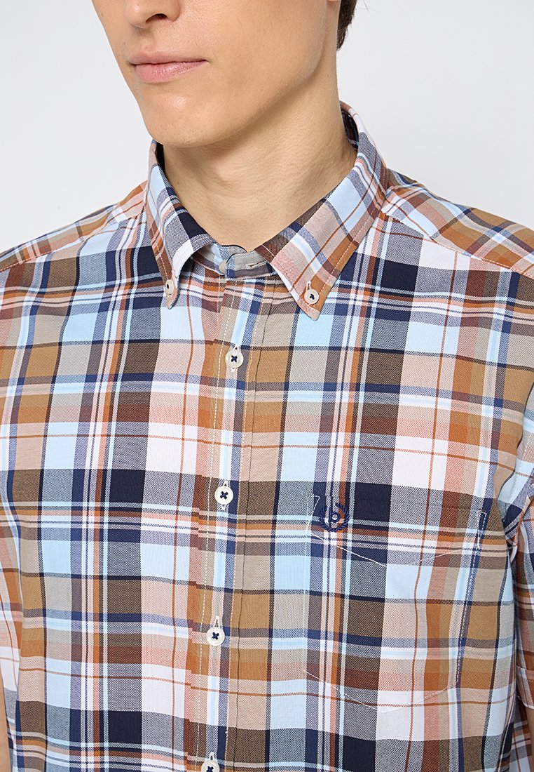 Camicia a quadri in beige, azzurro chiaro e blu navy. Presenta un colletto button-down, una tasca sul petto e bottoni bianchi. Tessuto in cotone.