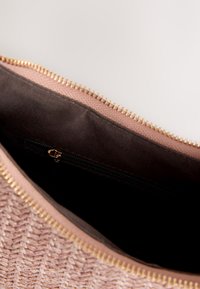 Sac tissé rose clair ouvert montrant l'intérieur en tissu noir avec une petite poche zippée et une fermeture à glissière dorée.