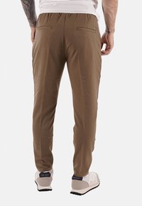 Pantaloni jogger marroni, elasticizzati, con vita elasticizzata, due tasche posteriori e vestibilità affusolata, abbinati a sneakers chiari.