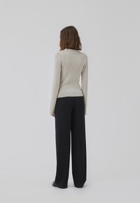Pull en maille côtelée beige clair avec une silhouette ajustée et des manches longues, associé à un pantalon noir à jambes larges, le tout sur un fond neutre.