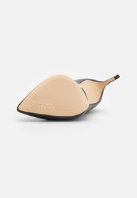 Zwarte puntige hak met een gladde oppervlakte, stiletto-hak en een lichtbeige rubberen zool met een gestructureerde grip en branding.
