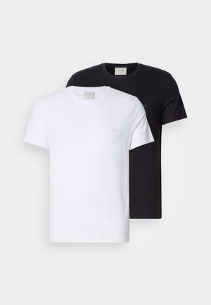 Deux t-shirts à col rond, un blanc et un noir, en coton doux. Les deux ont un design simple et un petit logo sur la poitrine.