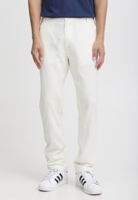 Witte linnen broek met een relaxte pasvorm, voorzien van zijzakken en een zachte textuur, gecombineerd met witte sneakers met zwarte strepen.