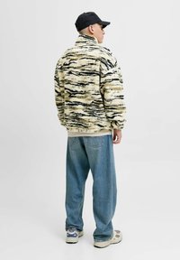 Fleecejacke mit hohem Kragen, cremefarbigem und schwarzem Tigermuster, kombiniert mit weit geschnittenen Jeans und hellen Sneakers.