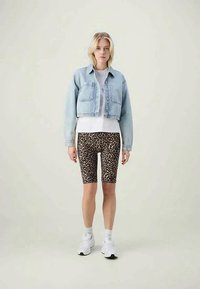 Lyseblå cropped denimjakke over en hvit t-skjorte, kombinert med leopardskinnsykler og hvite joggesko.