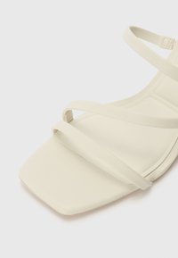 Light beige sandal featuring a square toe, thin straps, and a smooth texture. The design is minimalistic with no additional patterns or embellishments.
