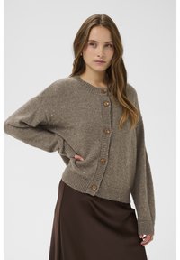 Rudas megztas kardiganas su apvalia iškirpte, dideliais mediniais mygtukais ir subtiliomis metalinėmis siūlėmis visame audinyje. Laisvo silueto.