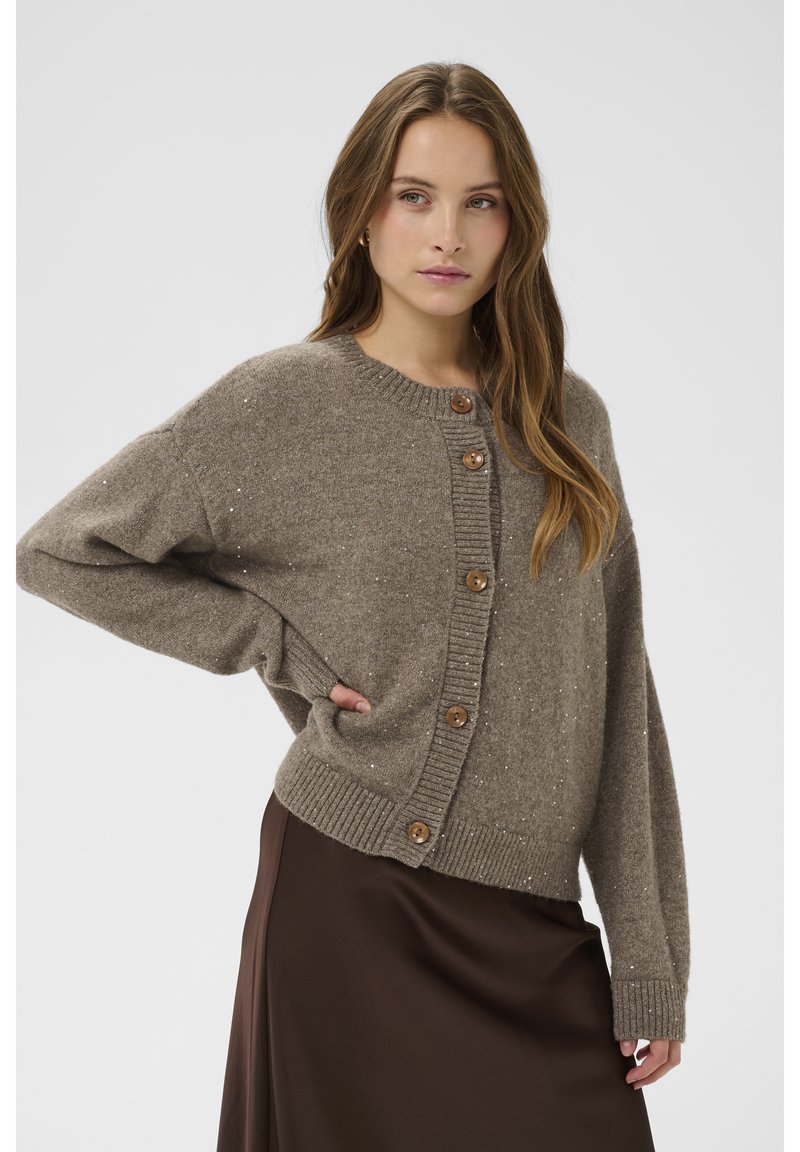 Rudas megztas kardiganas su apvalia iškirpte, dideliais mediniais mygtukais ir subtiliomis metalinėmis siūlėmis visame audinyje. Laisvo silueto.
